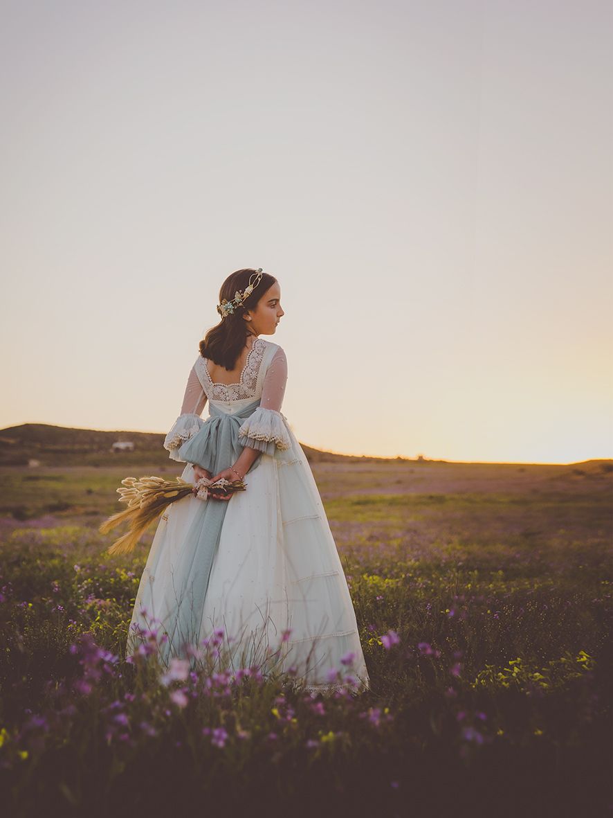 Niña de comunión de pie en un campo de flores moradas al atardecer en los campos de Cabo de Gata.