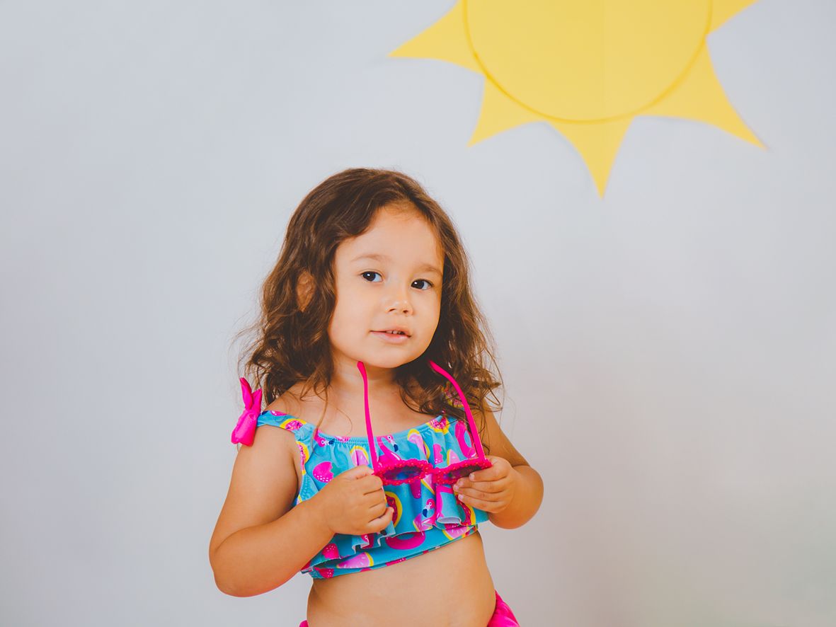 Fotografía de una pequeña sujetando sus gafas de sol con un top azul y fucsia en su reportaje de estudio de verano.