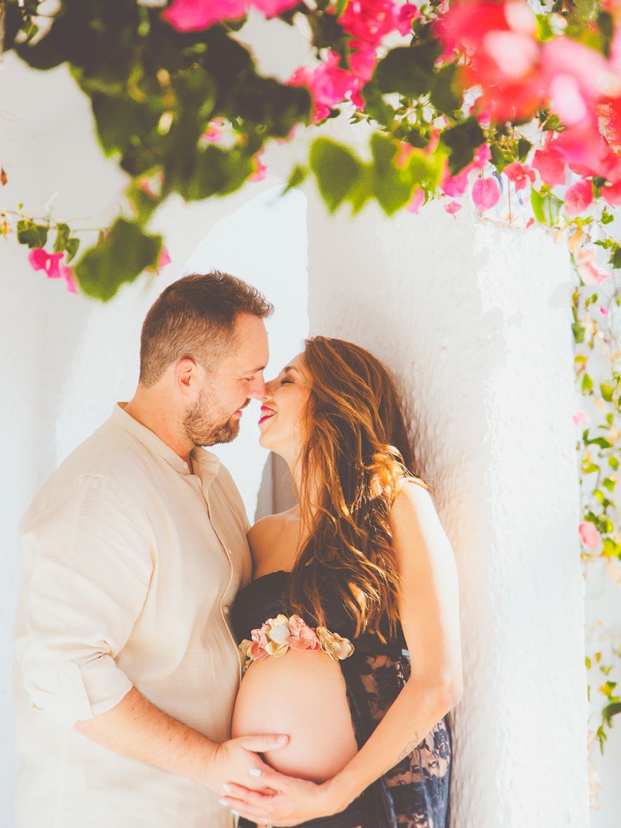 Una pareja comparte un momento romántico bajo unas buganvillas rosas durante una sesión de fotos de maternidad en Almería.