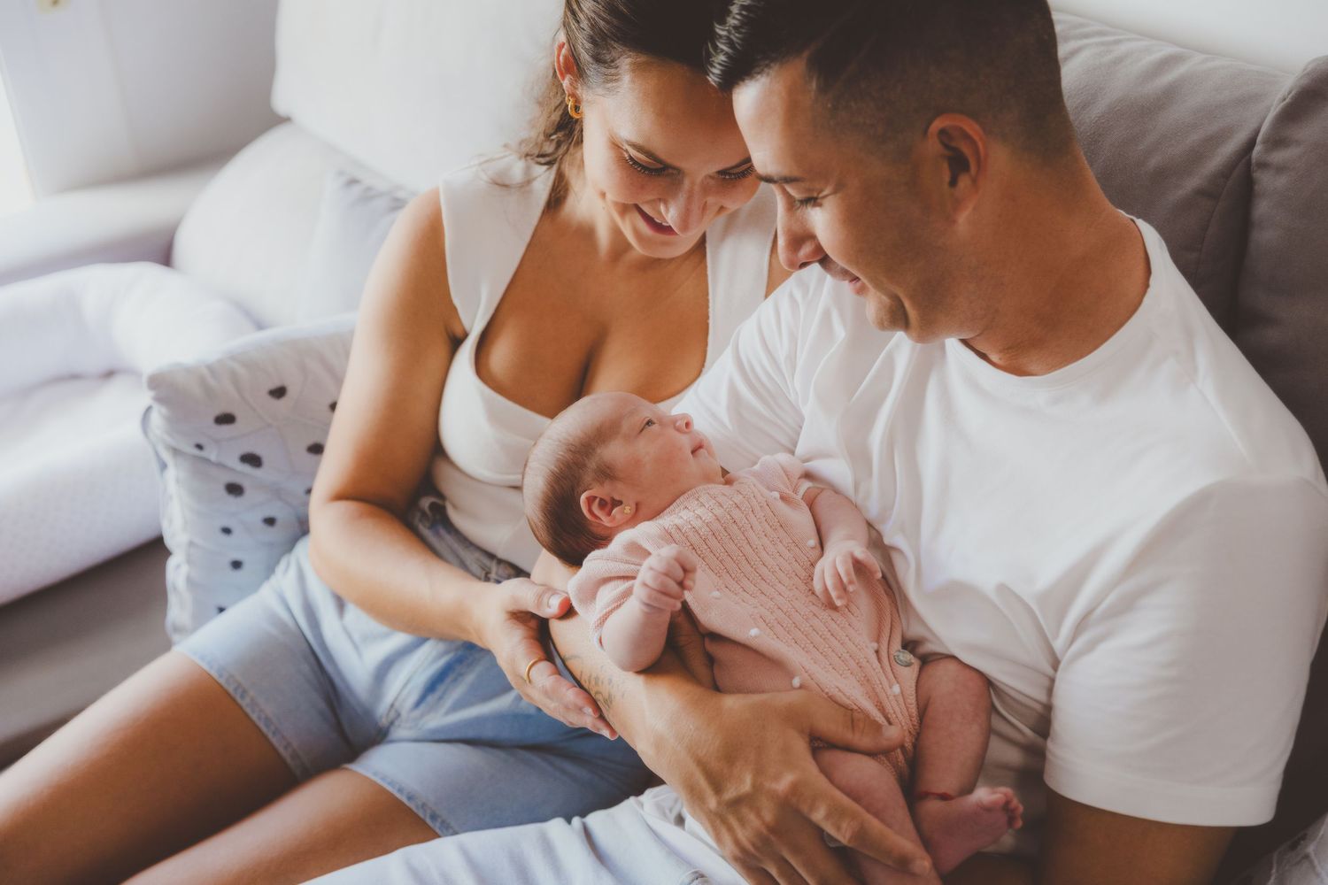 Unos papás felices sentados con su bebé recién nacido en el reportaje fotográfico realizado en su casa muy luminosa.