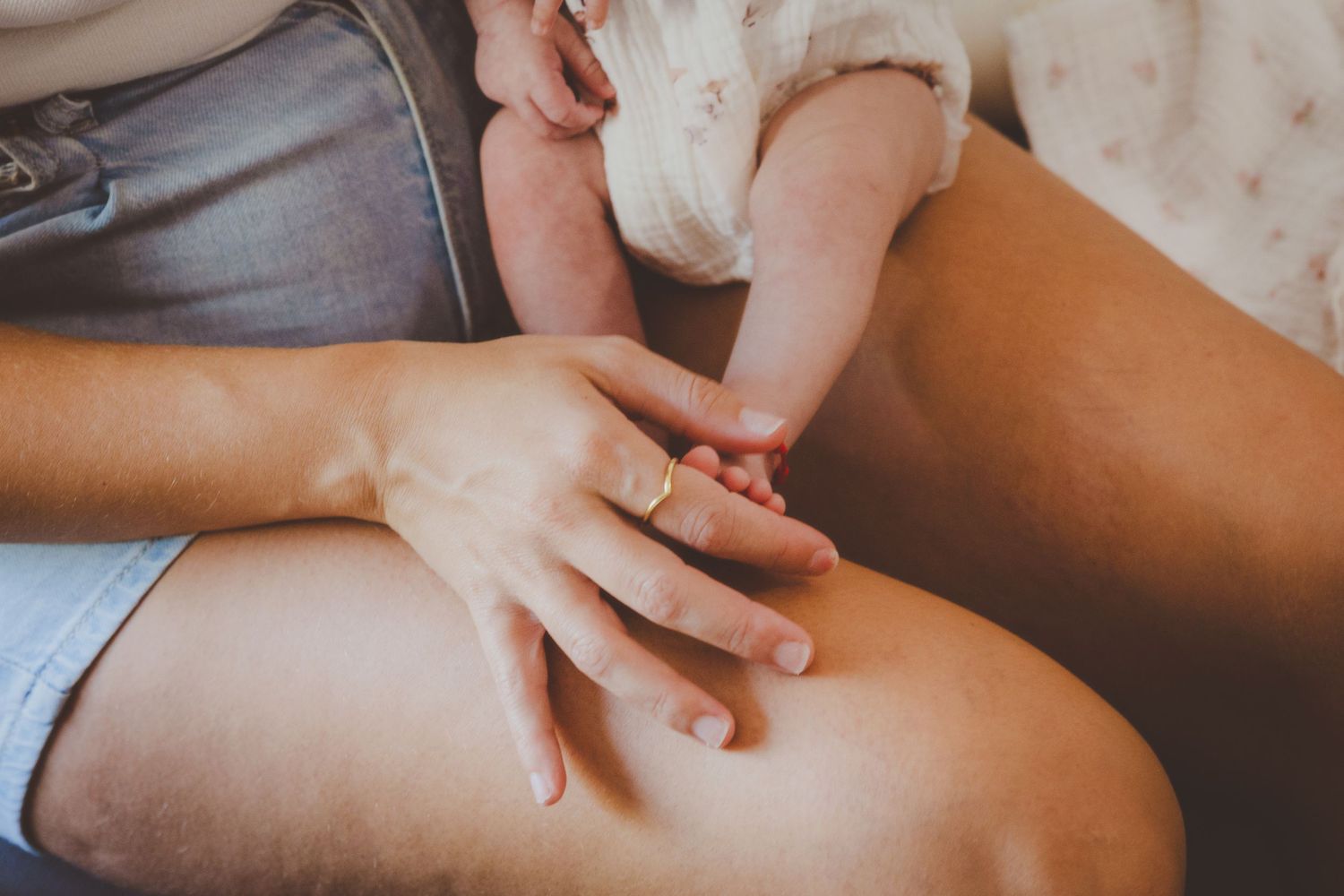 Primer plano de la mano de una madre con un anillo, sujetando los deditos del pie de su bebé recién nacido en su reportaje de fotos.