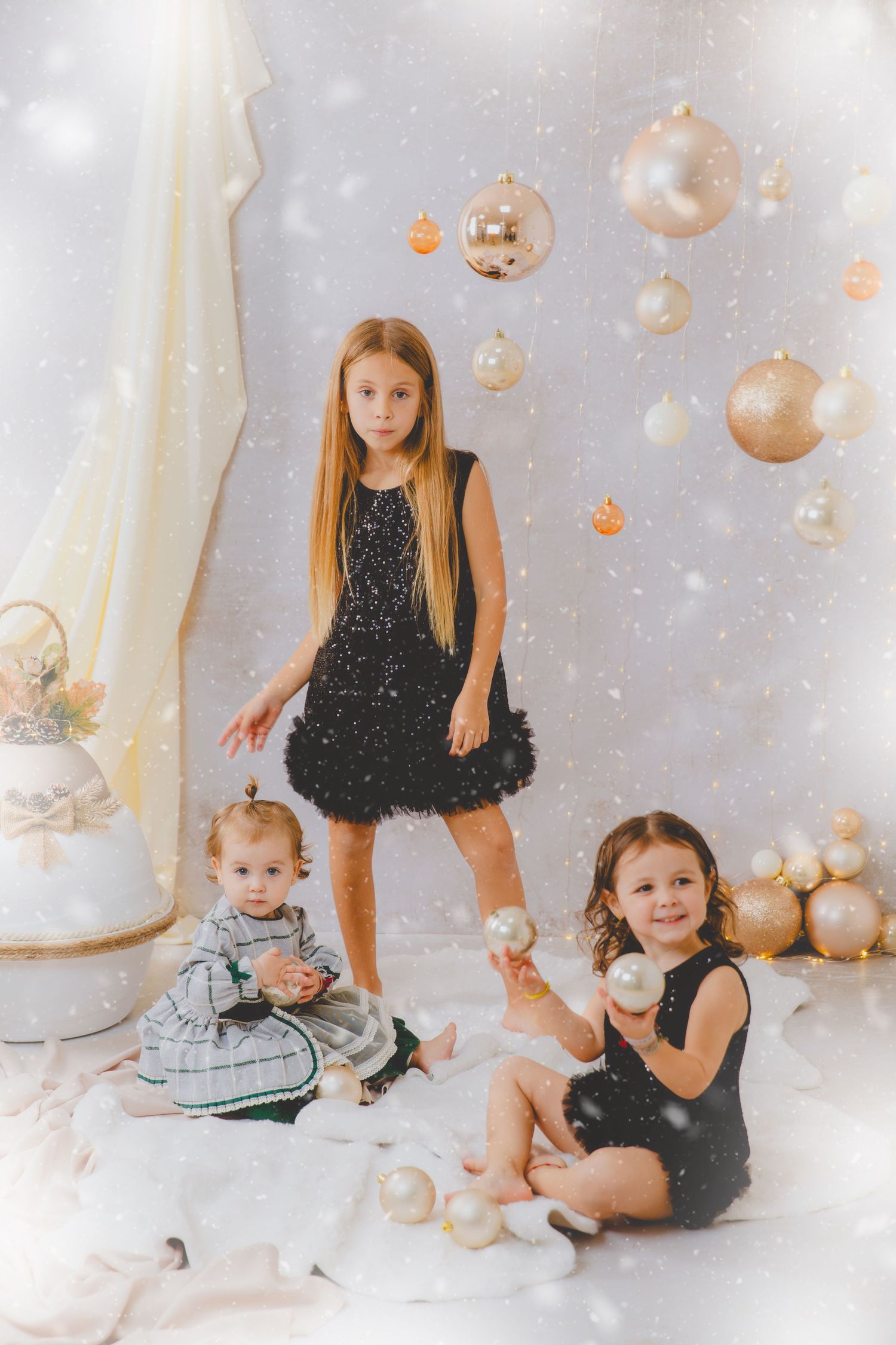 Tres hermanas con vestidos negros posan con adornos navideños dorados en un ambiente elegante y luminoso.