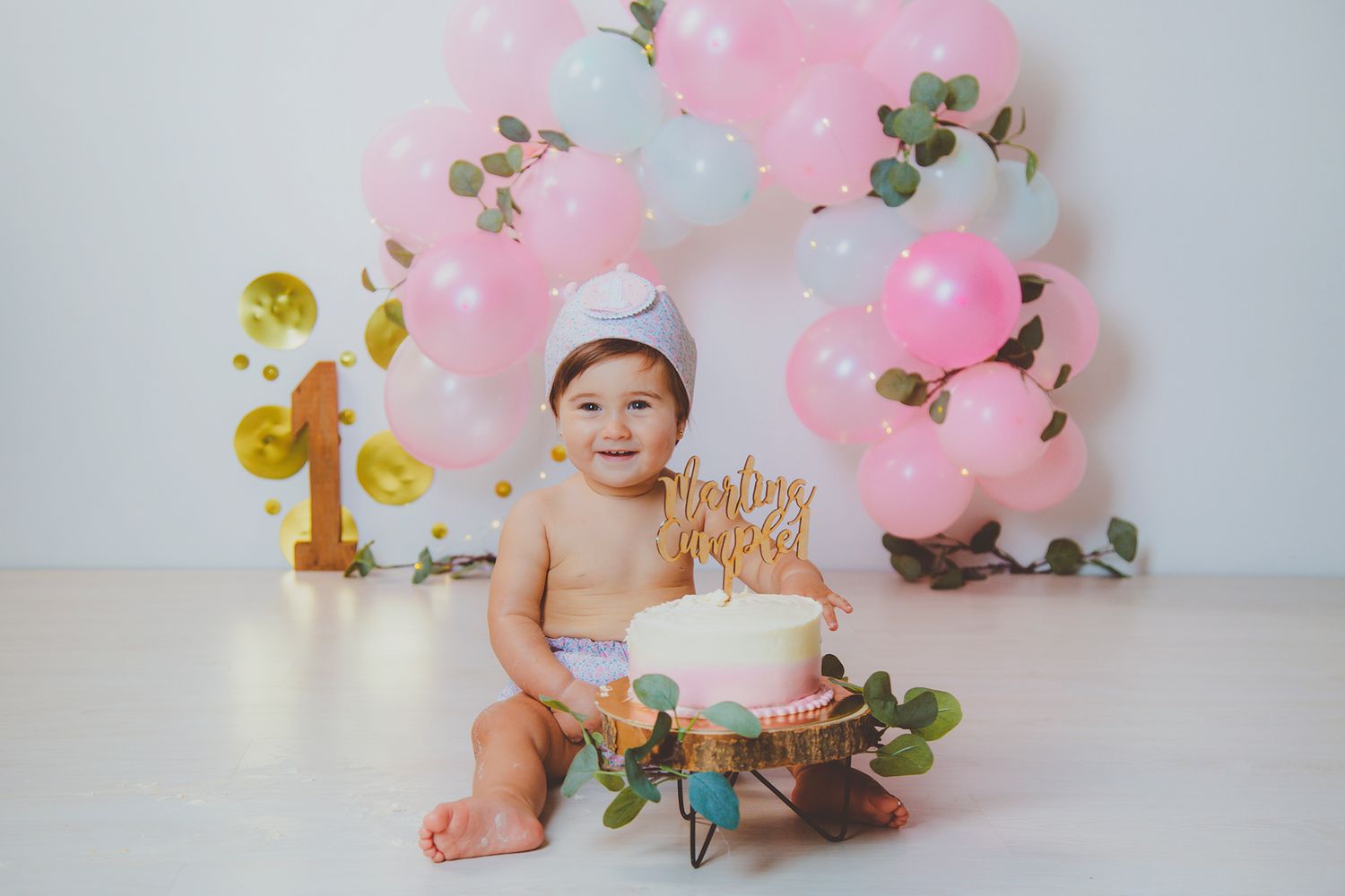 Bebé sonriente con corona sujetando su tarta de primer cumpleaños durante su sesión de smash cake.