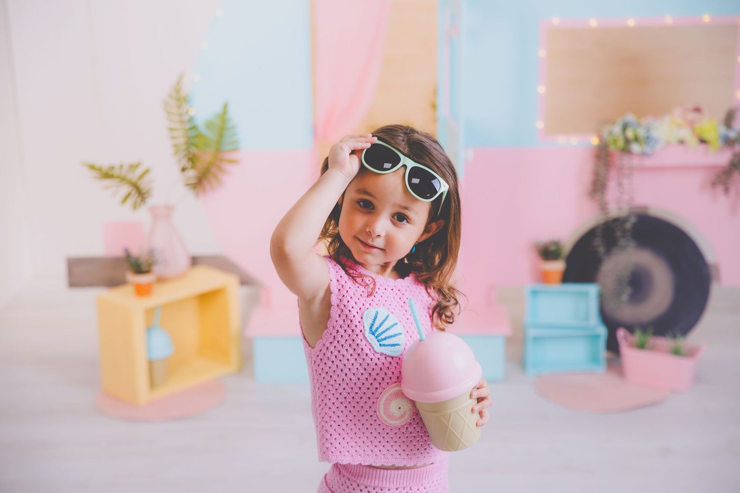 Niña posando para su sesión de fotos de verano con un vestido rosa mientras se coloca las gafas de sol.