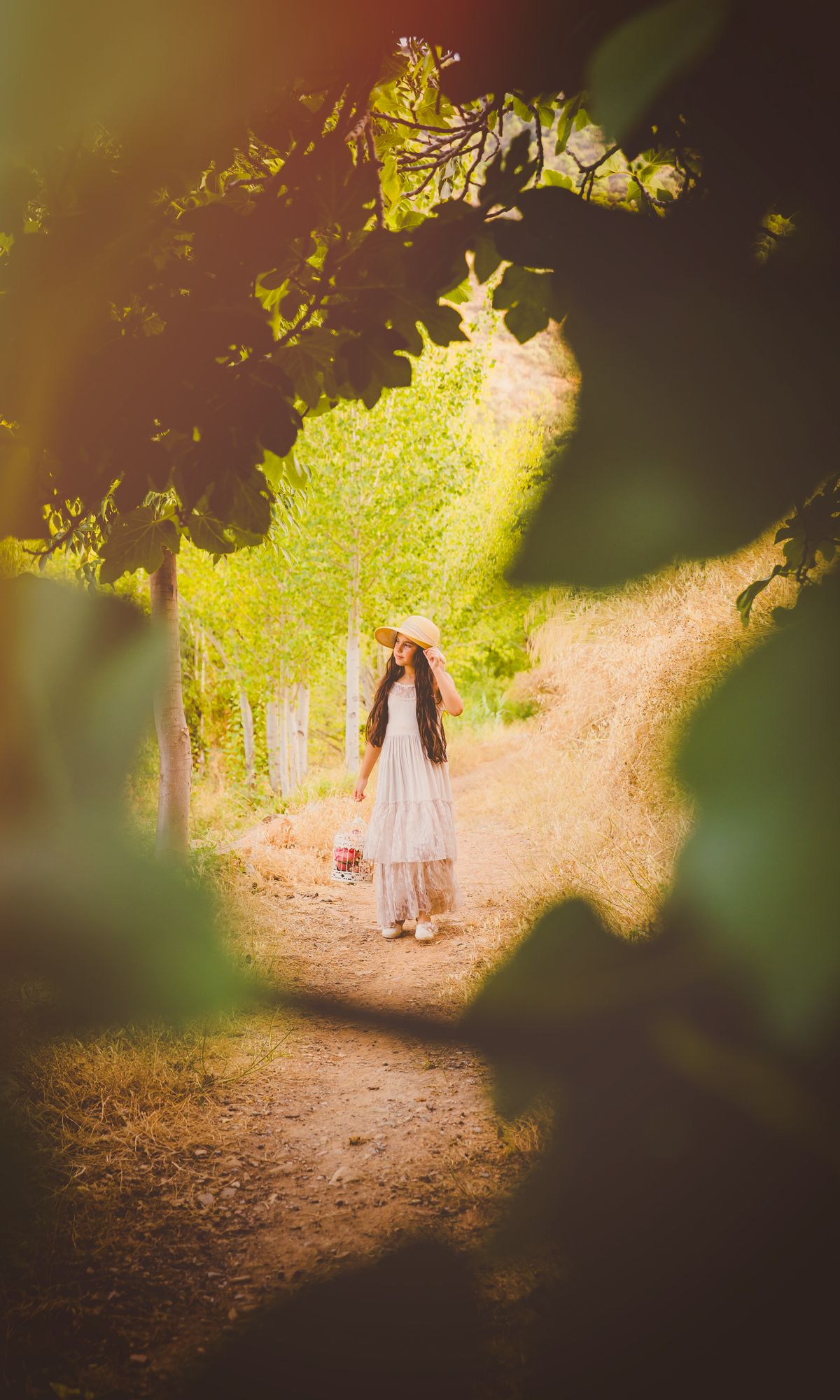 Imagen de una pequeña con vestido y sombrero blancos caminando por un sendero soleado en el bosque en su reportaje de exteriores en Almería.