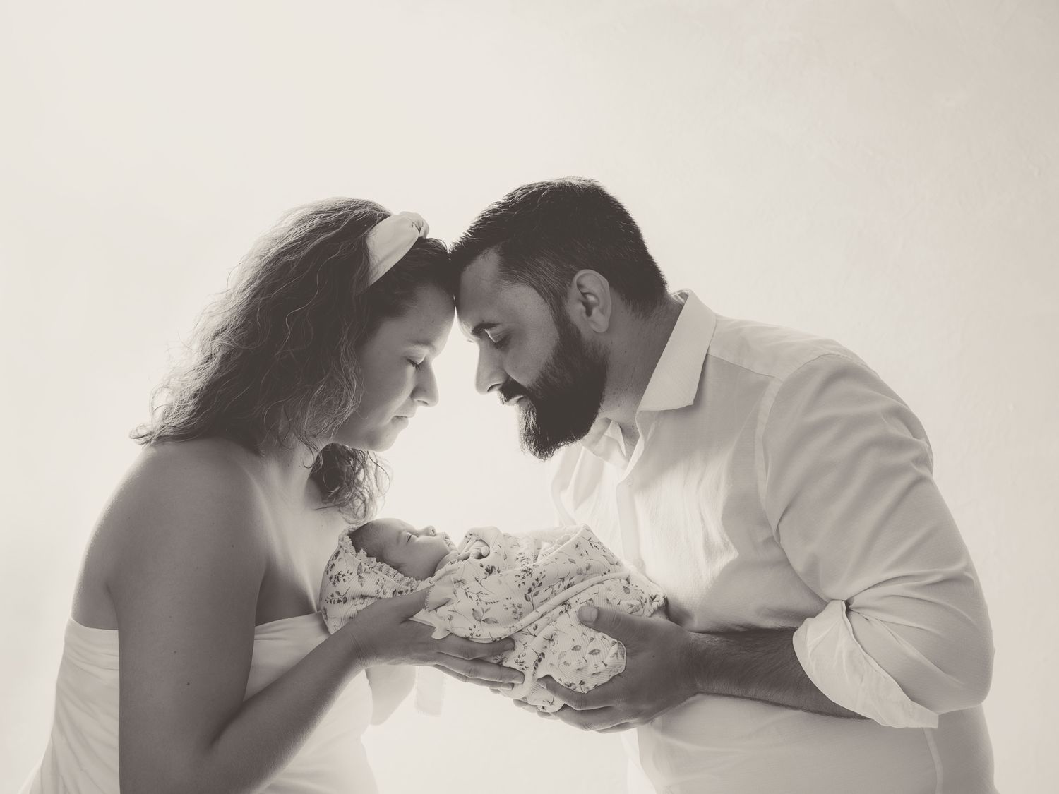 Fotografía en blanco y negro de unos papás que miran con ternura a su bebé recién nacido.