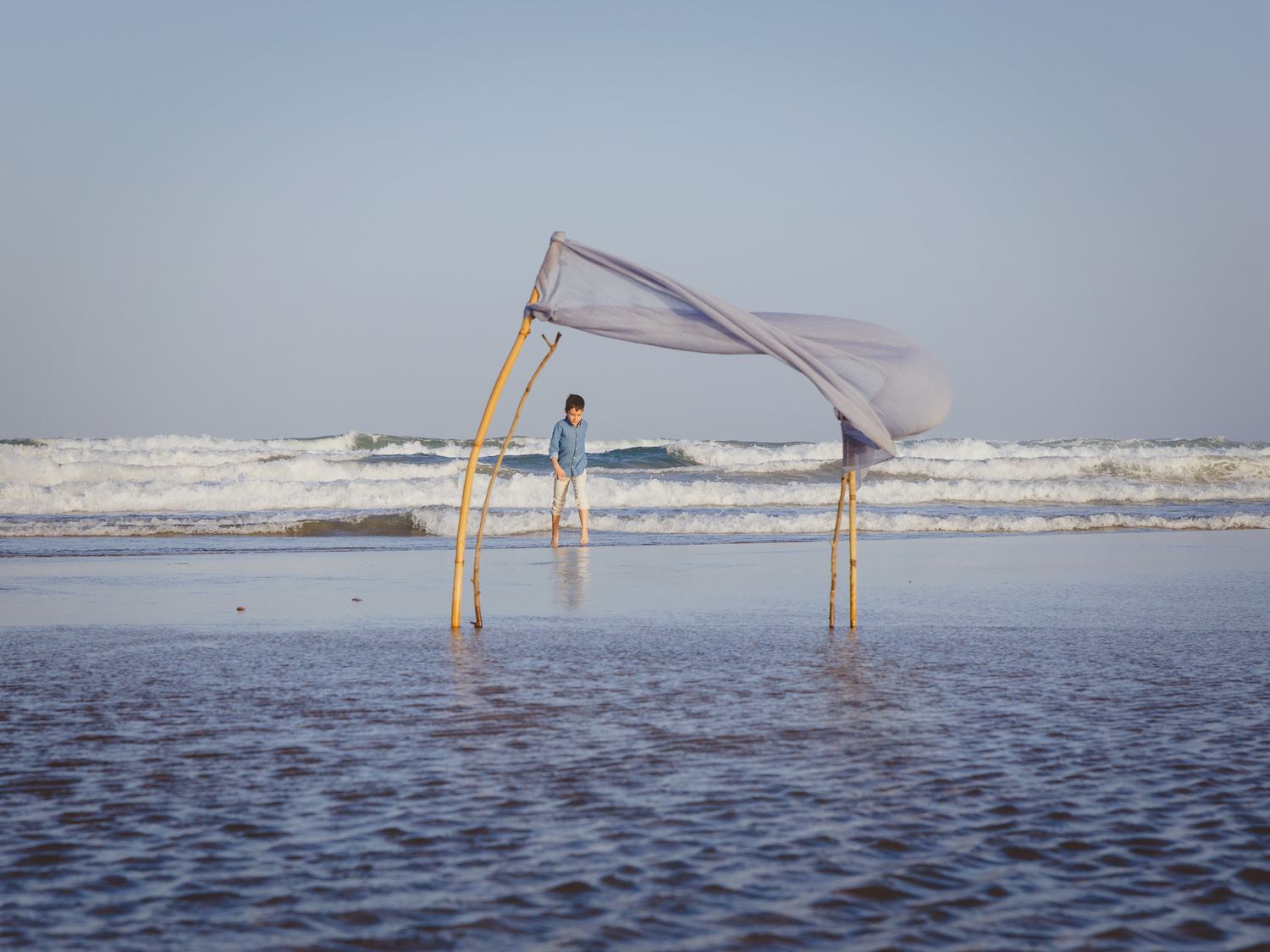 Fotografía de exteriores de comunión de un niño en el mar de Cabo de Gata, enmarcado en una estructura de tela que ondea con el viento.