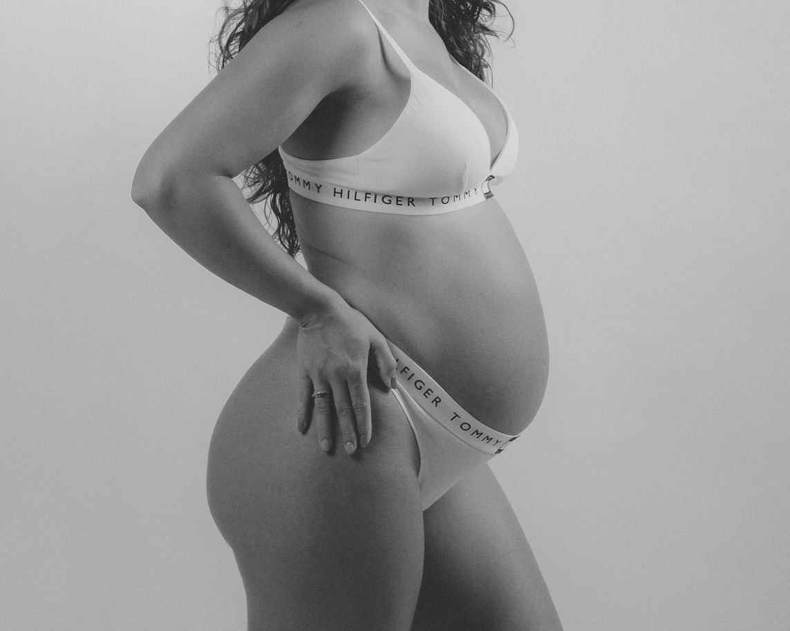Fotografía en blanco y negro de la barriga de una embarazada con un conjunto de ropa interior.