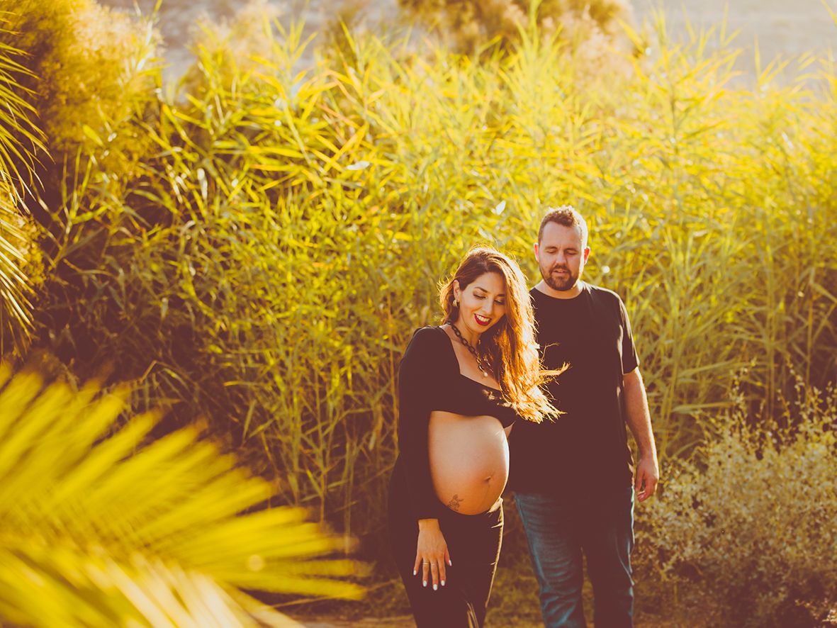 Pareja paseando junta en un campo bañado por la luz dorada del sol durante una sesión de fotos de maternidad en exteriores.