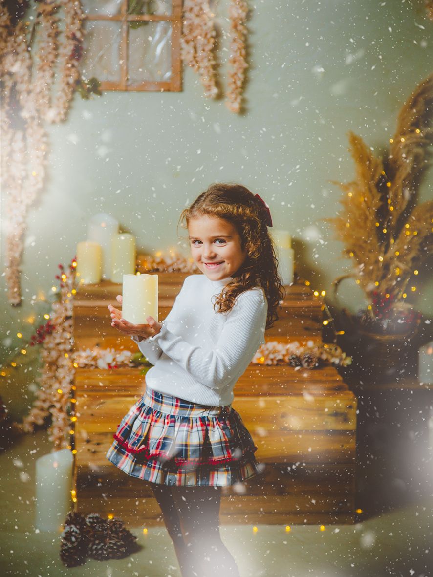 Preciosa niña sujeta una vela en un decorado de Navidad en su sesión de fotos.