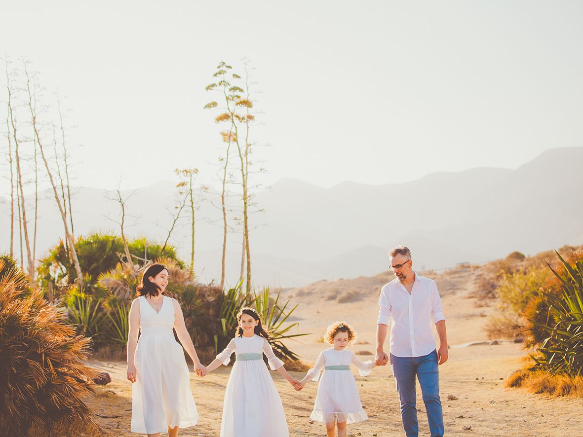 Familia de cuatro personas caminando de la mano en un paisaje desértico en Almería, un día de sesión de comunión soleado.