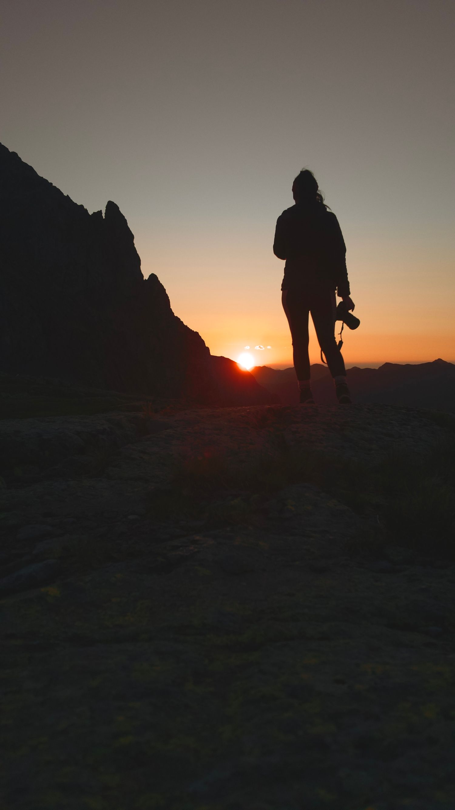Silueta de Paqui Rodríguez, fotógrafa apasionada por la naturaleza, contemplando un atardecer de montaña con su cámara.