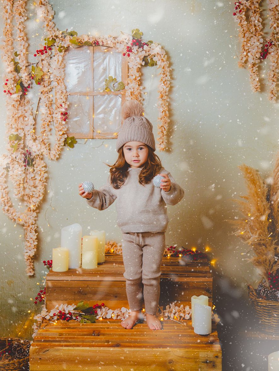 Decorado de Navidad donde se ve a una niña pequeña de pie al lado de velas y en una estructura de madera.