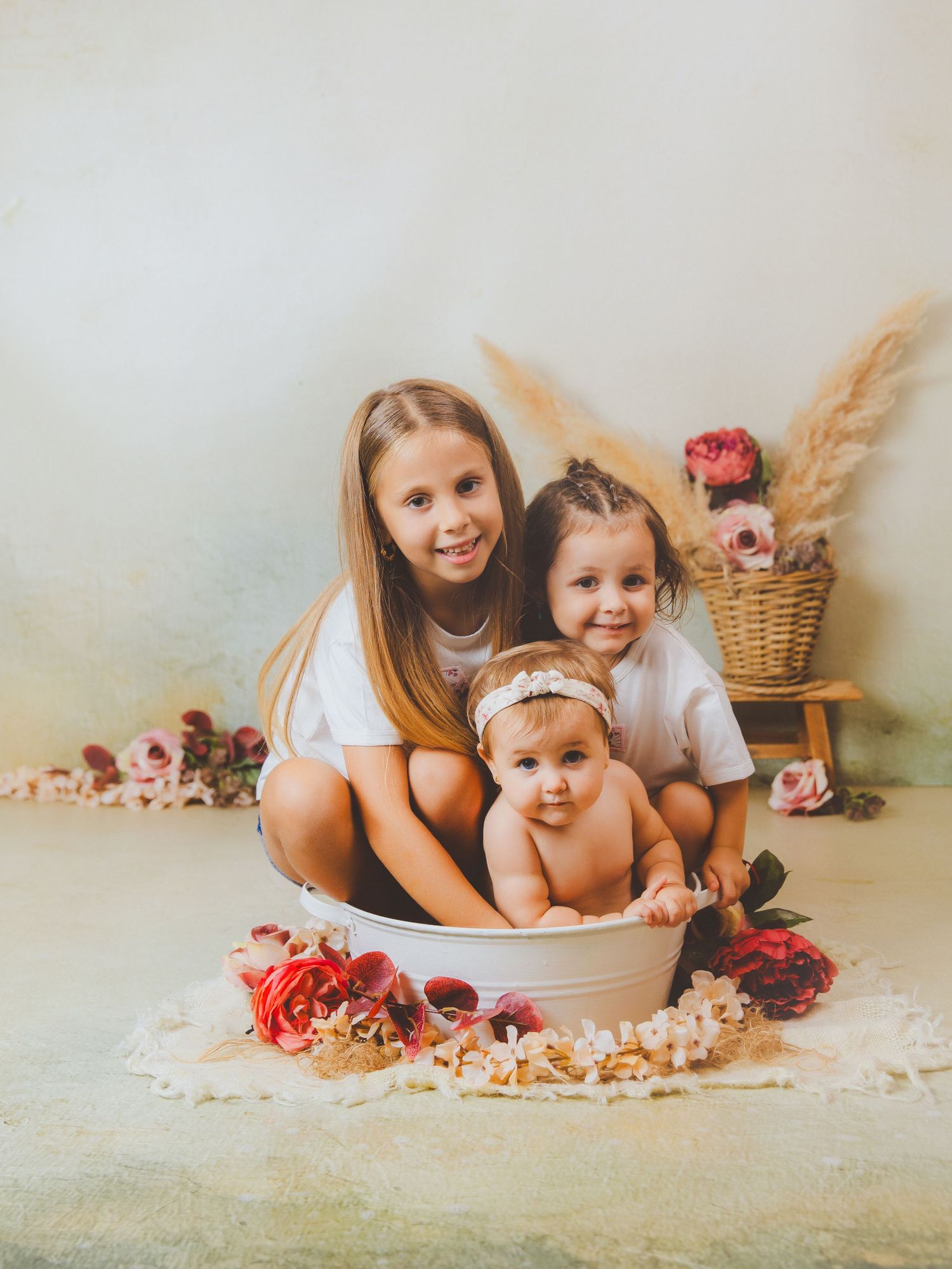 Tres hermanas posan juntas en una bañera blanca rodeada de decoraciones florales rojas y rosas con decoración bohemia.