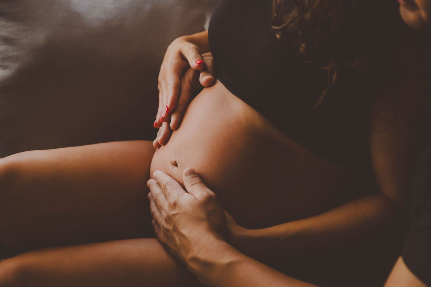 Foto de primer plano de una mujer embarazada que toca su barriga junto a las manos de su pareja.
