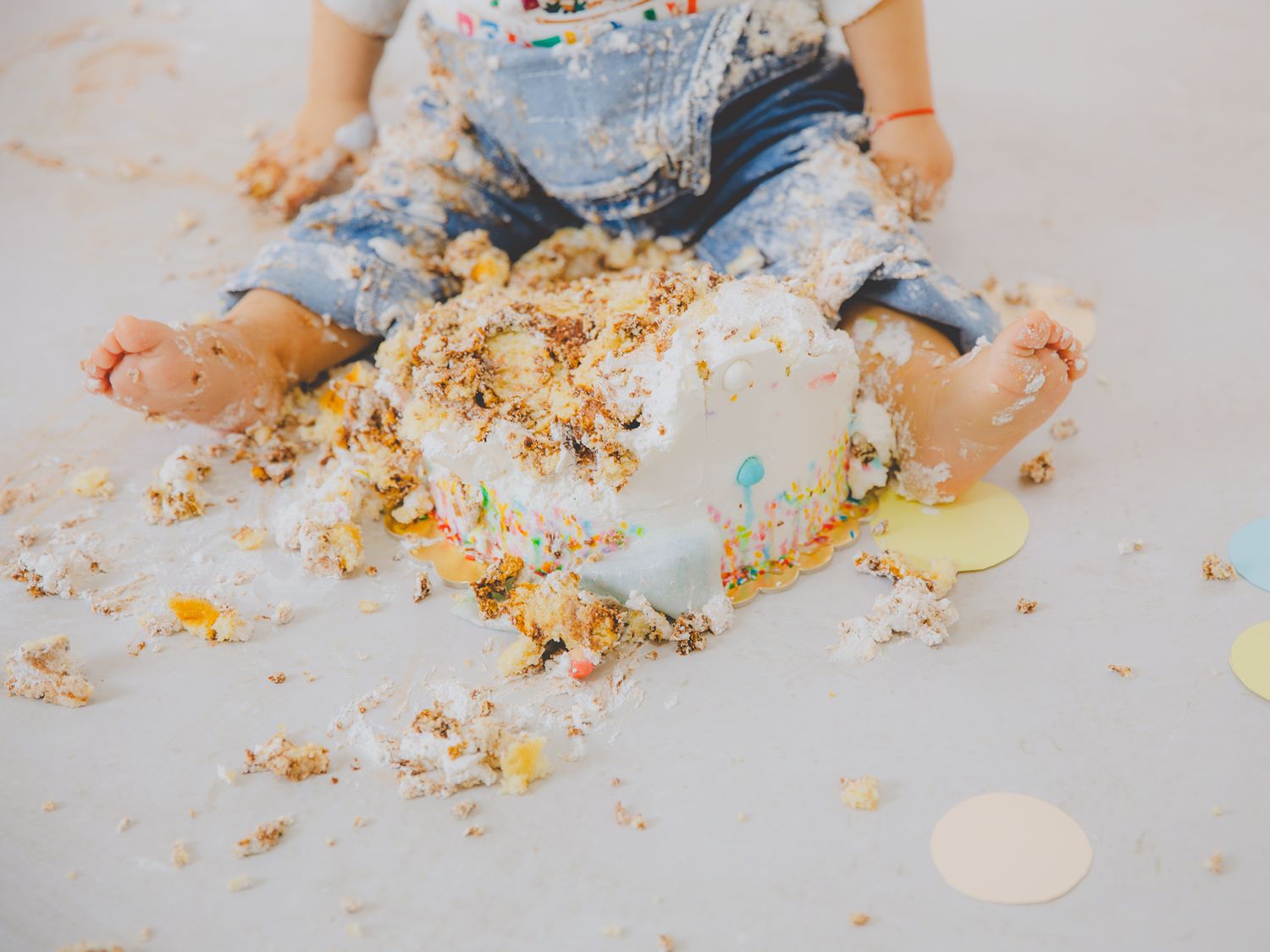 Detalle de los pies del bebé cubierto de pastel de cumpleaños aplastado, sentado en el suelo durante una sesión de fotos.
