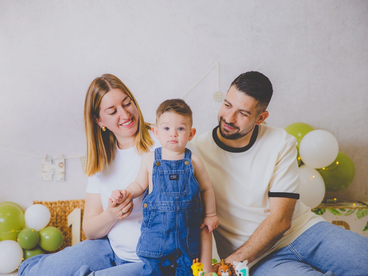 Familia feliz con un bebé vestido con un mono vaquero celebrando su primer cumpleaños con globos.