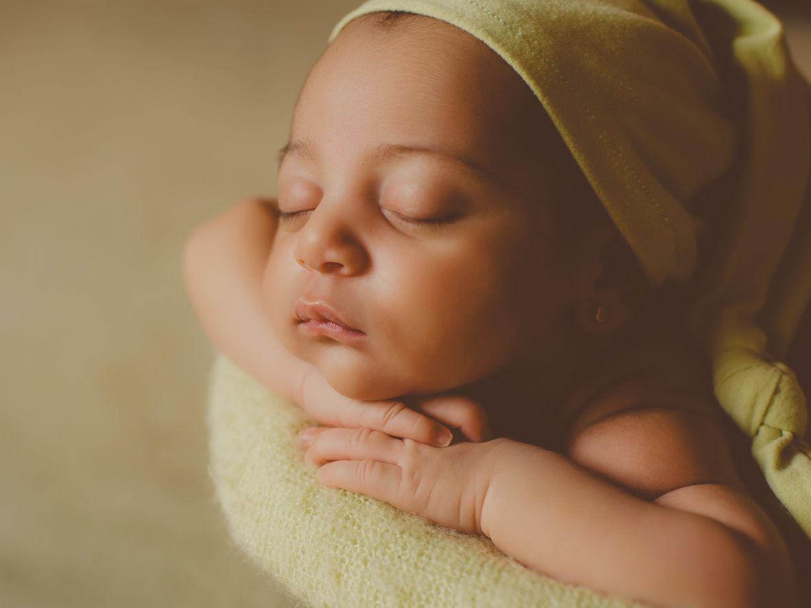 Fotografía de estudio de un bebé recién nacido sereno, descansando sobre una manta verde y con un suave gorro.