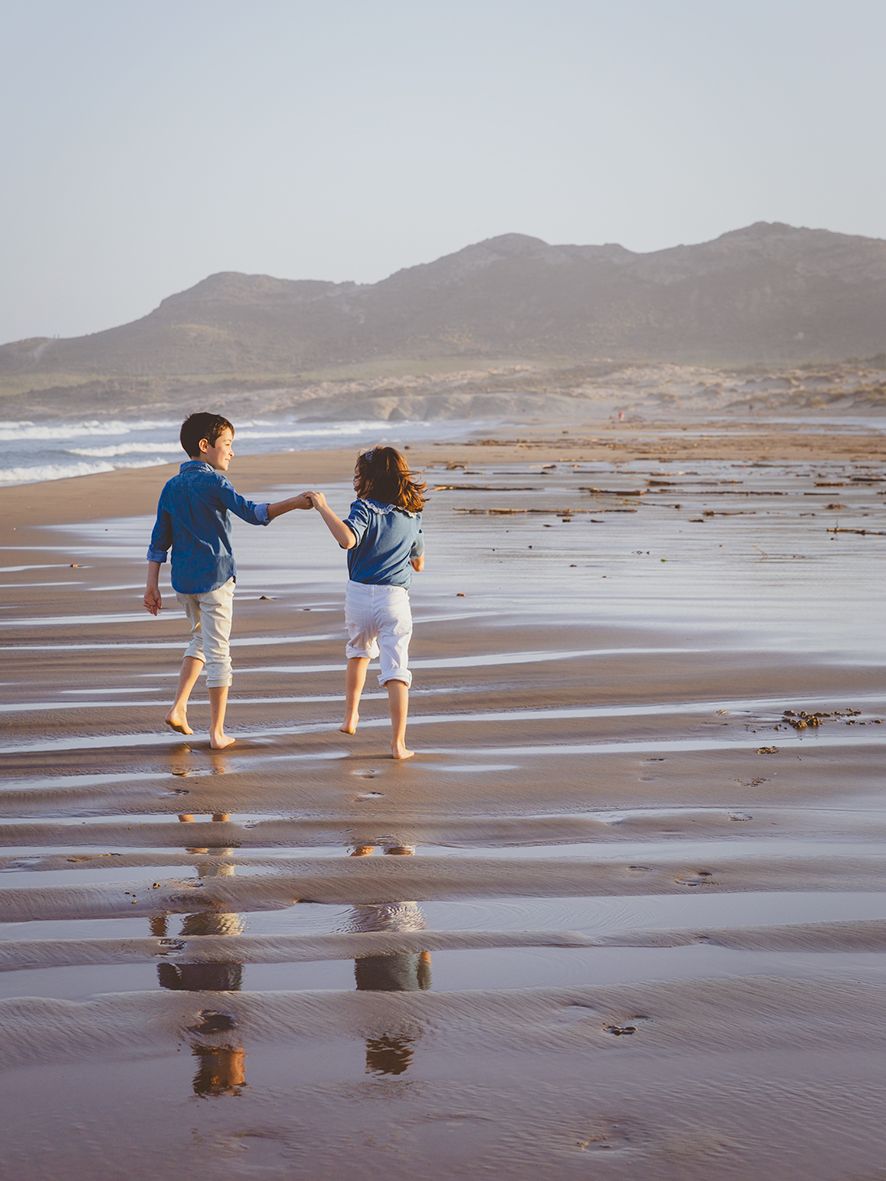 Fotografía de dos hermanos cogidos de la mano caminando por la orilla de la playa de Genoveses en Almería.