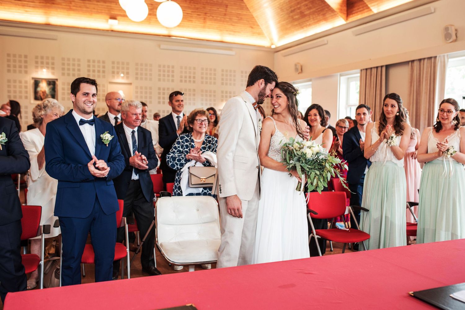 Wedding party and guests gather in an elegant reception room with red carpet.