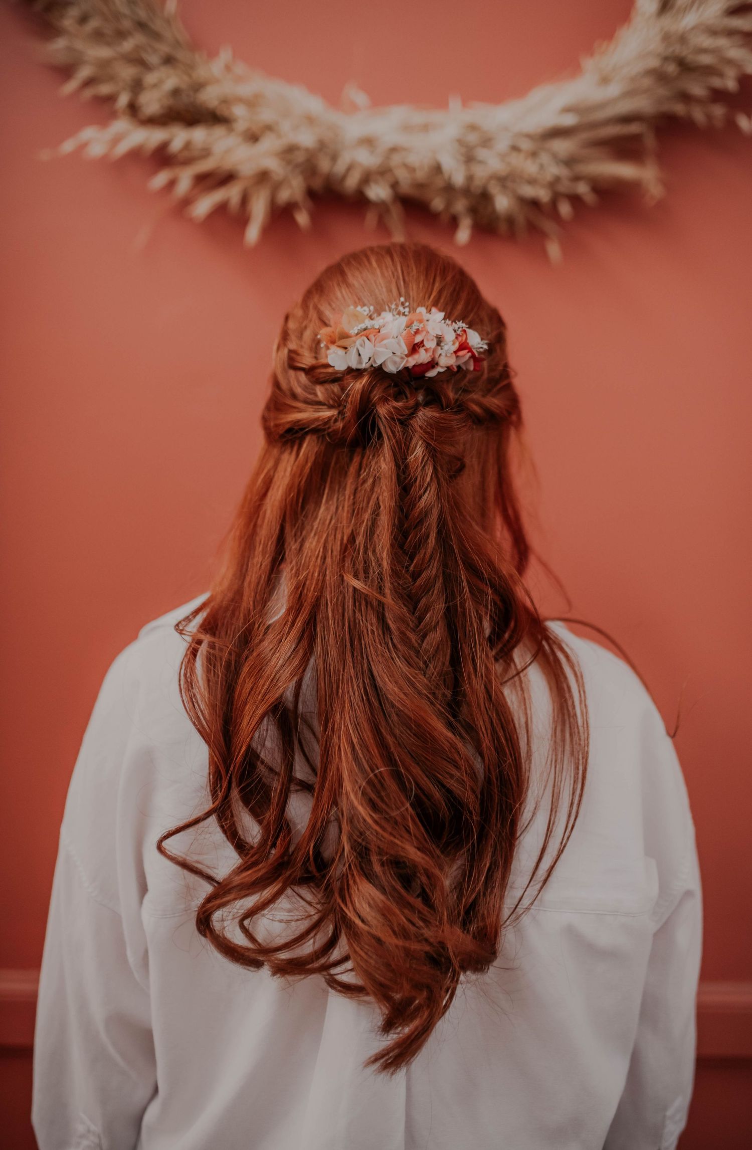 Close-up of bridal hairstyle with red hair and delicate hair accessories against coral background.