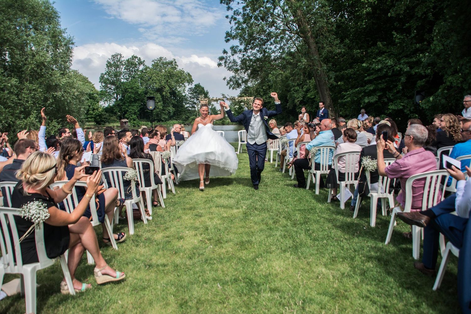 Outdoor wedding ceremony setup with white chairs on a grassy hill under blue skies.