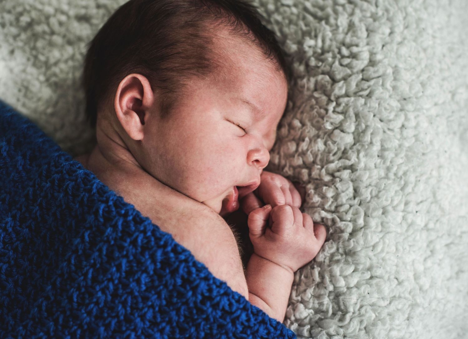 Sleeping newborn on textured gray blanket in natural light.