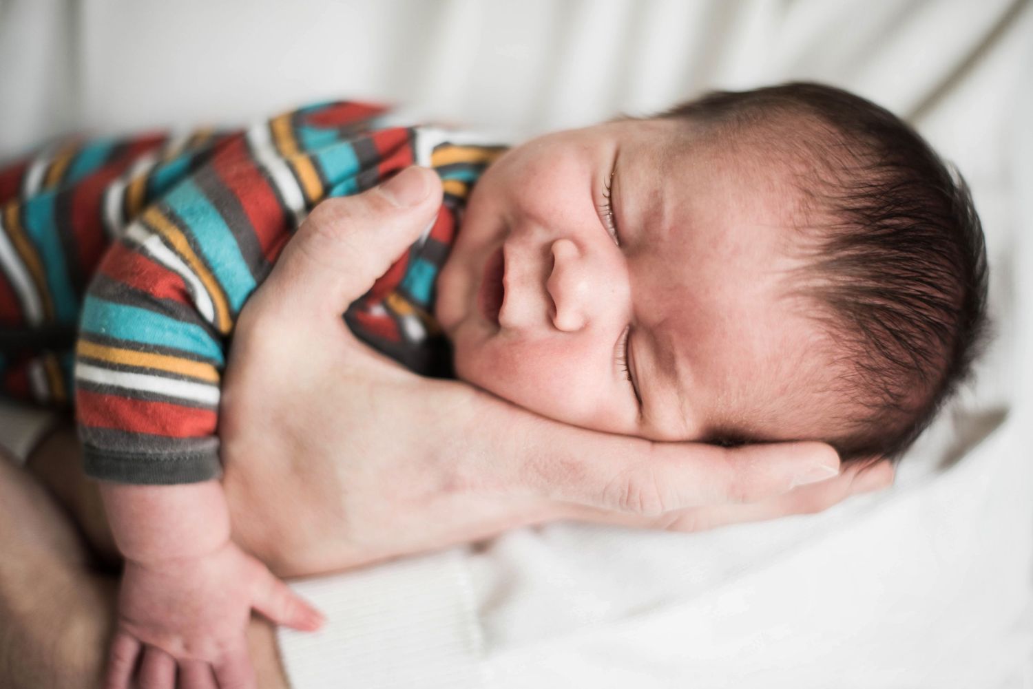 Newborn baby sleeping peacefully on white bedding wearing striped outfit.