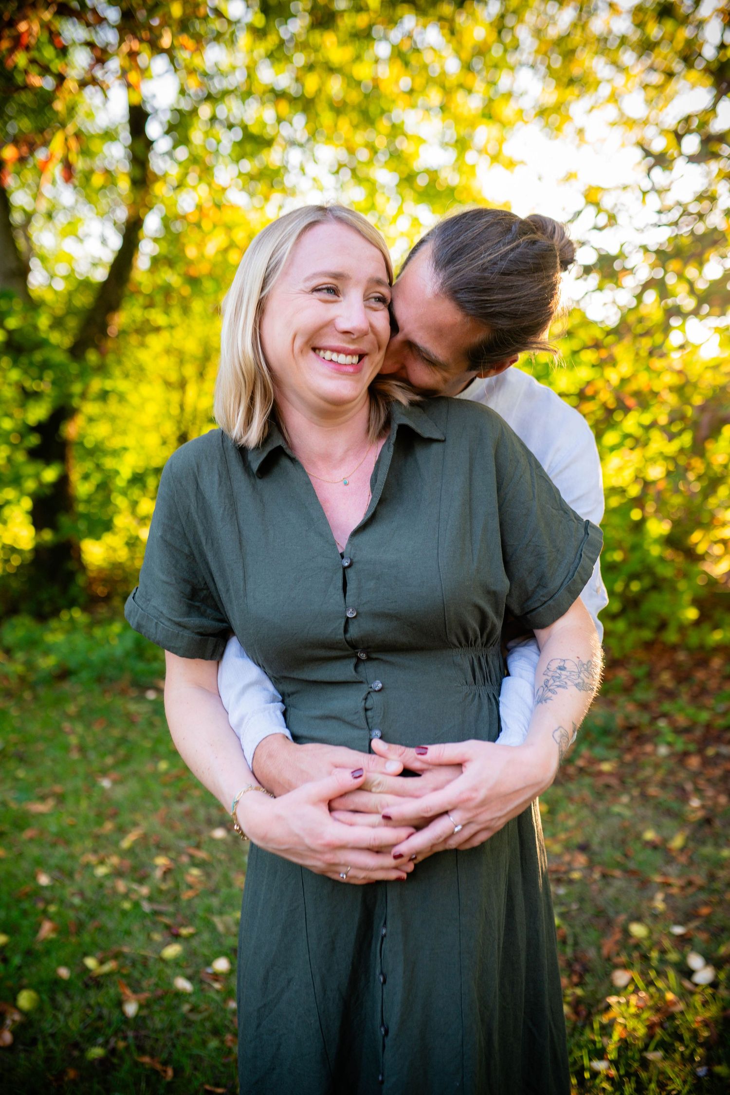 Romantic autumn maternity photos with golden sunlight filtering through trees in the background.
