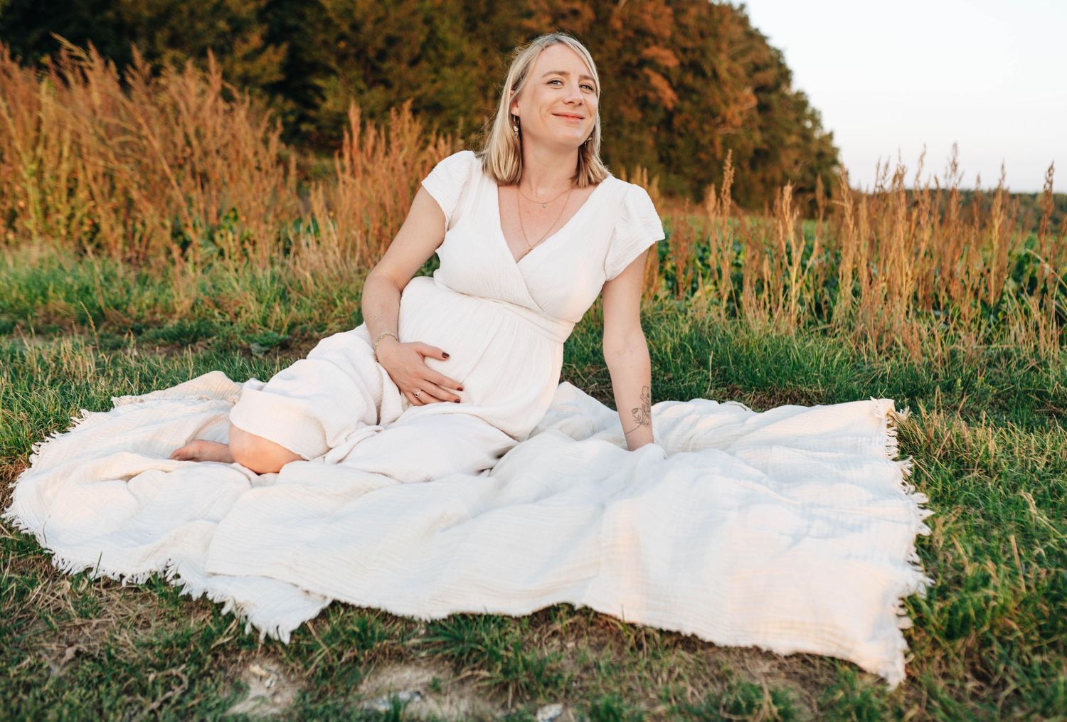 Artistic maternity photos taken in a field during sunset with flowing white fabric.