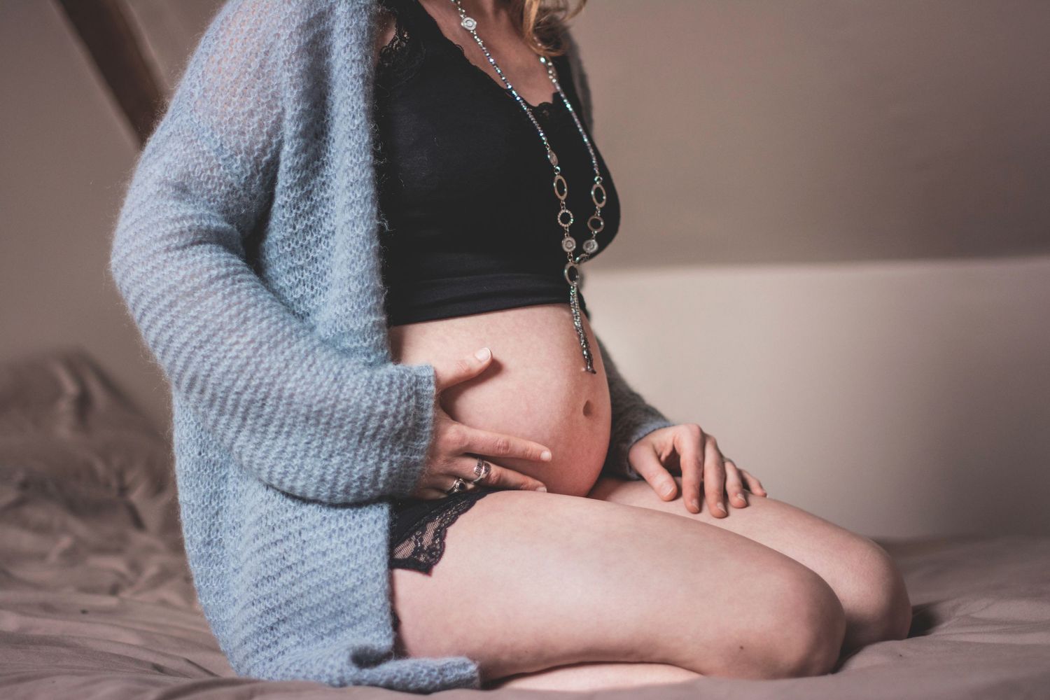 Artistic maternity boudoir photos showing pregnant belly with soft gray sweater.