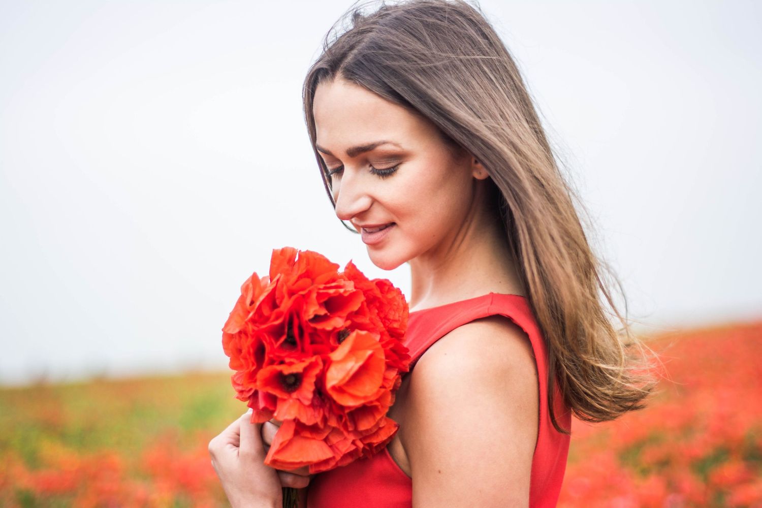 Summer portrait holding a bouquet of bright red poppies against a light background.
