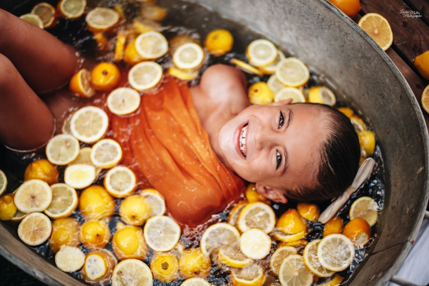 Creative portrait in metal tub filled with floating citrus slices and warm lighting.