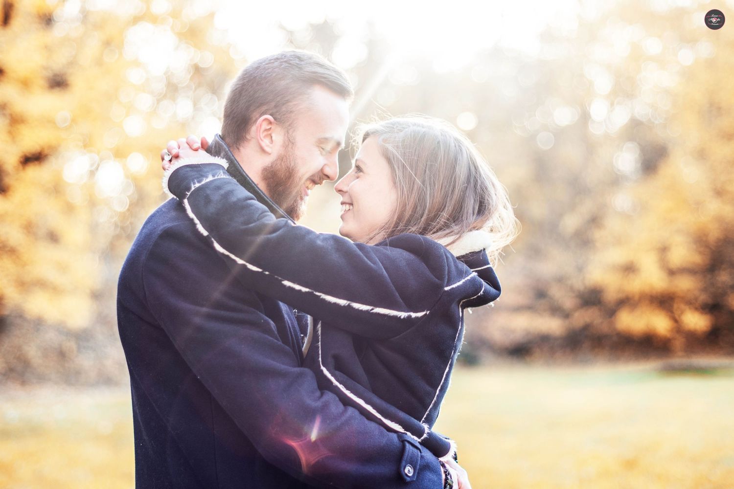 Couple embracing in golden autumn sunlight during an outdoor photo session.
