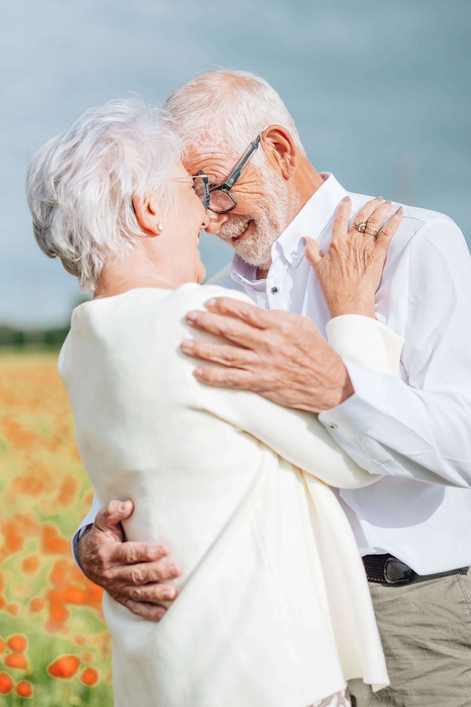 Senior couple embracing and nearly kissing in a vibrant poppy field, sharing a romantic moment outdoors.