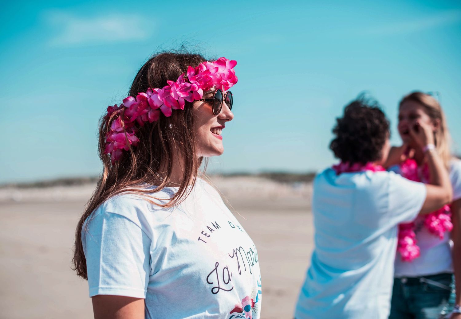 Women in white t-shirts walking along the beach with pink flower accessories.