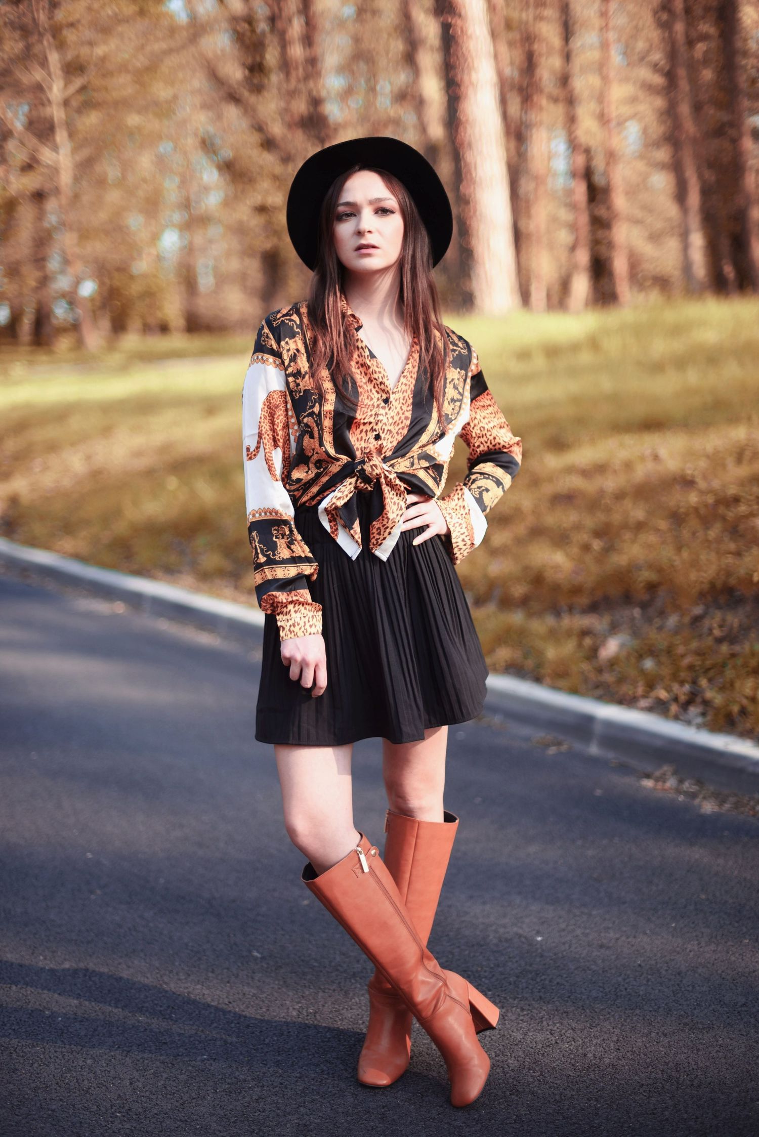 Autumn fashion outfit featuring brown boots, black skirt and patterned top on a rural road.