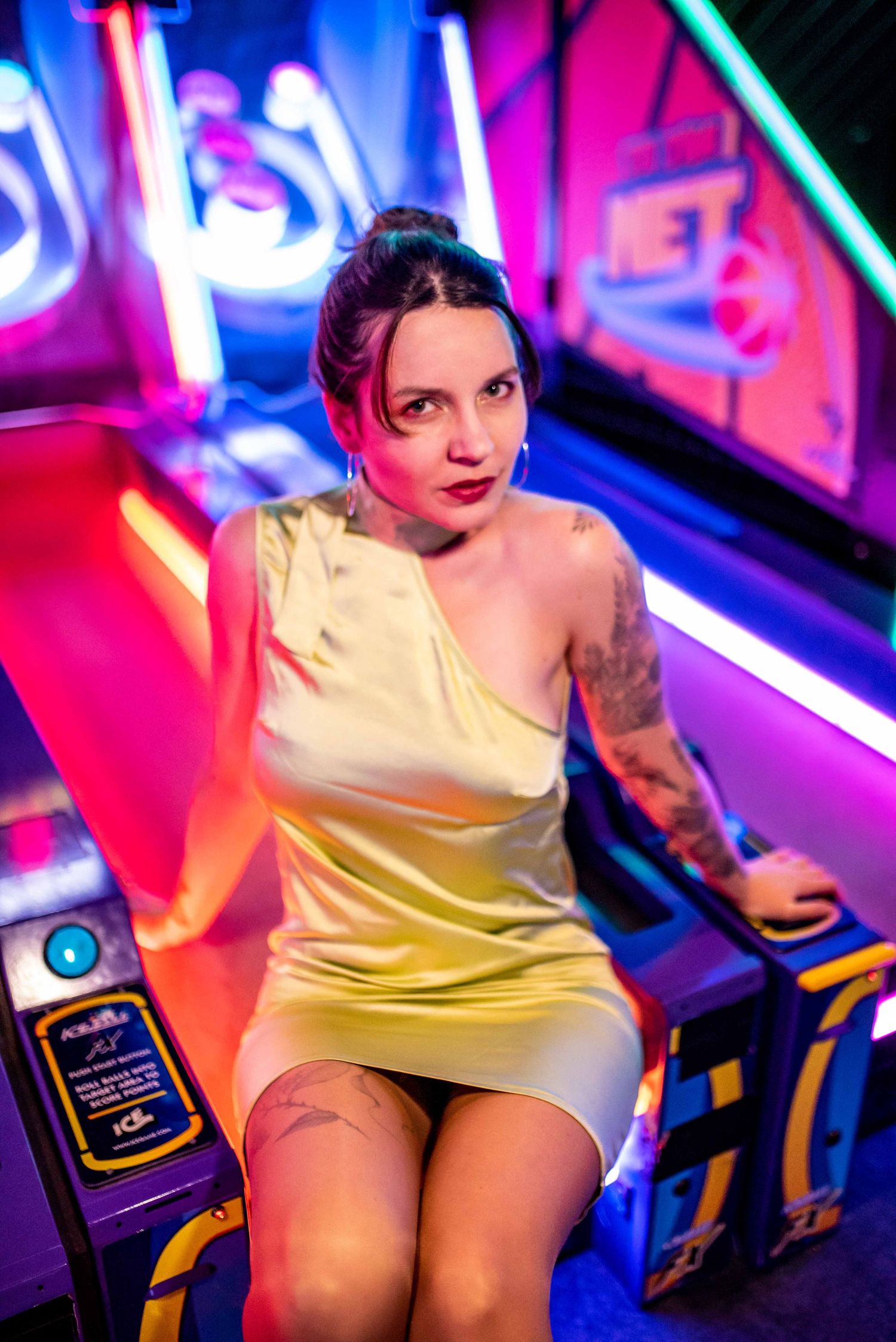 Fashion model in yellow dress posing with neon lights in arcade setting.