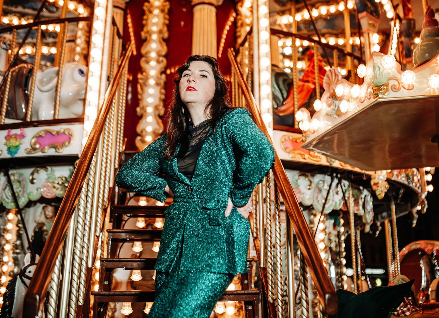 Glamorous photoshoot with sparkling green dress against carnival lights and carousel poles.