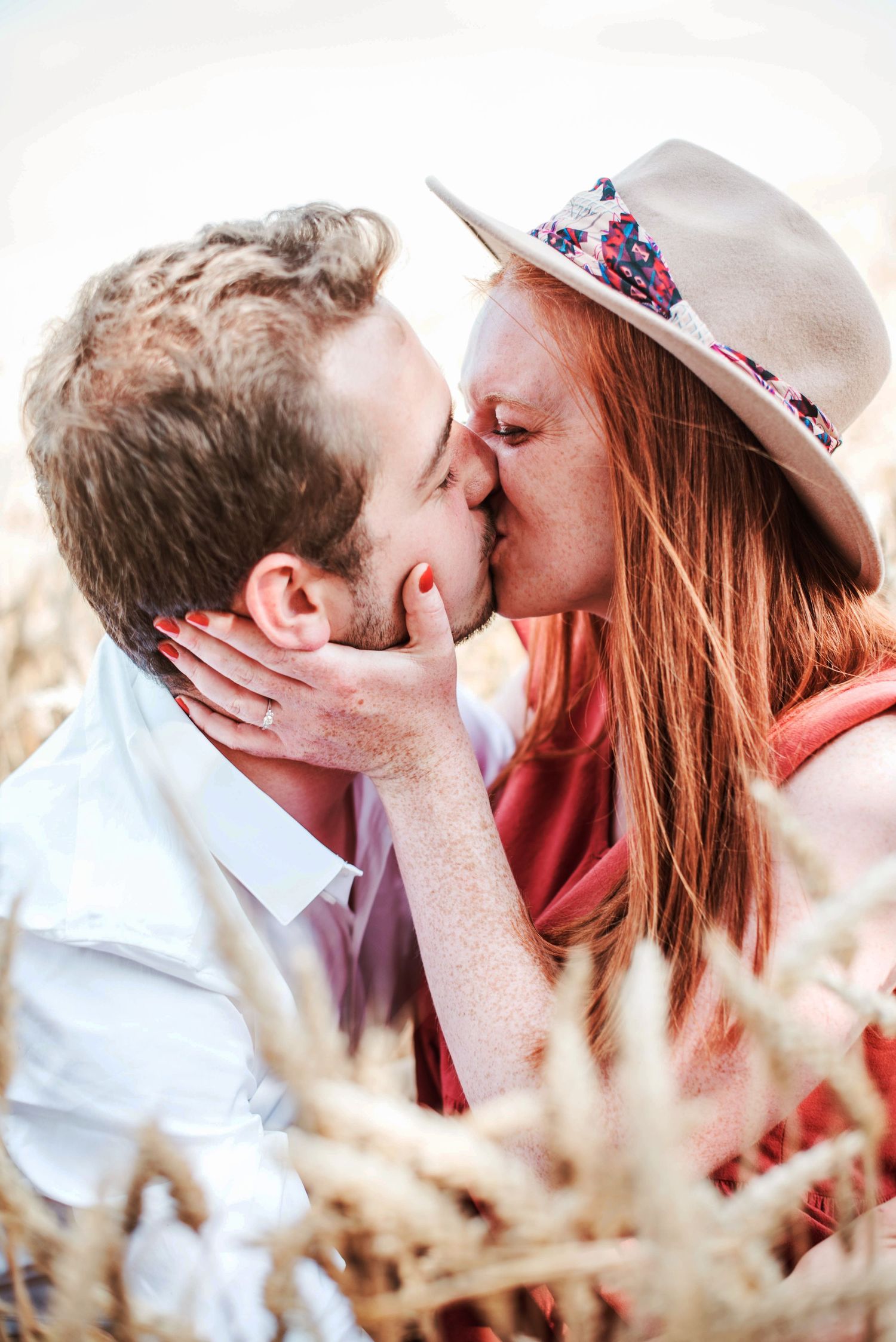 Couple sharing romantic kisses in wheat field wearing white and coral outfits.