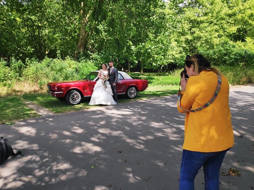 Photography session in park with vintage car visible in background.