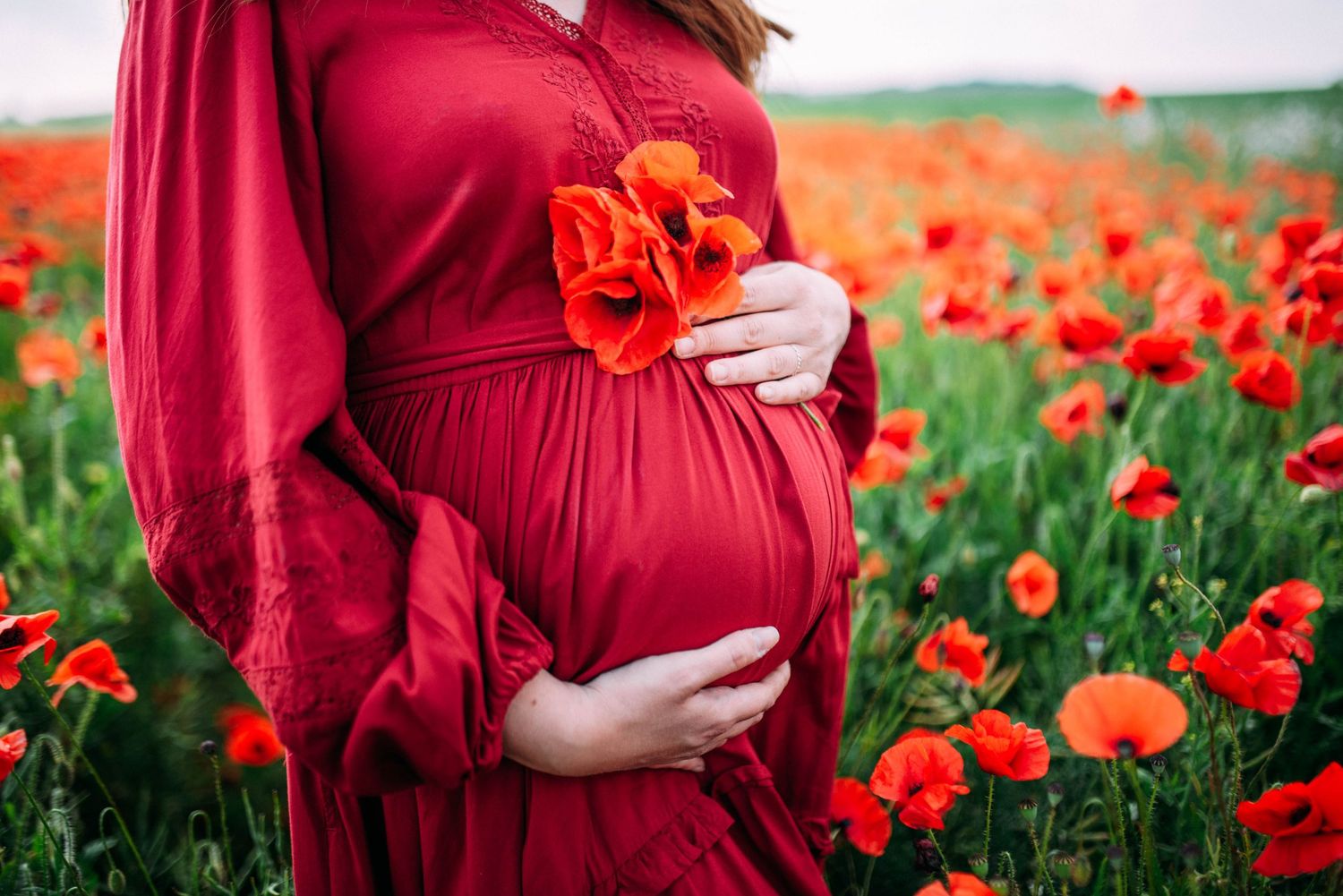 A red flowing dress contrasts beautifully against a field of bright orange poppies in this maternity photo.