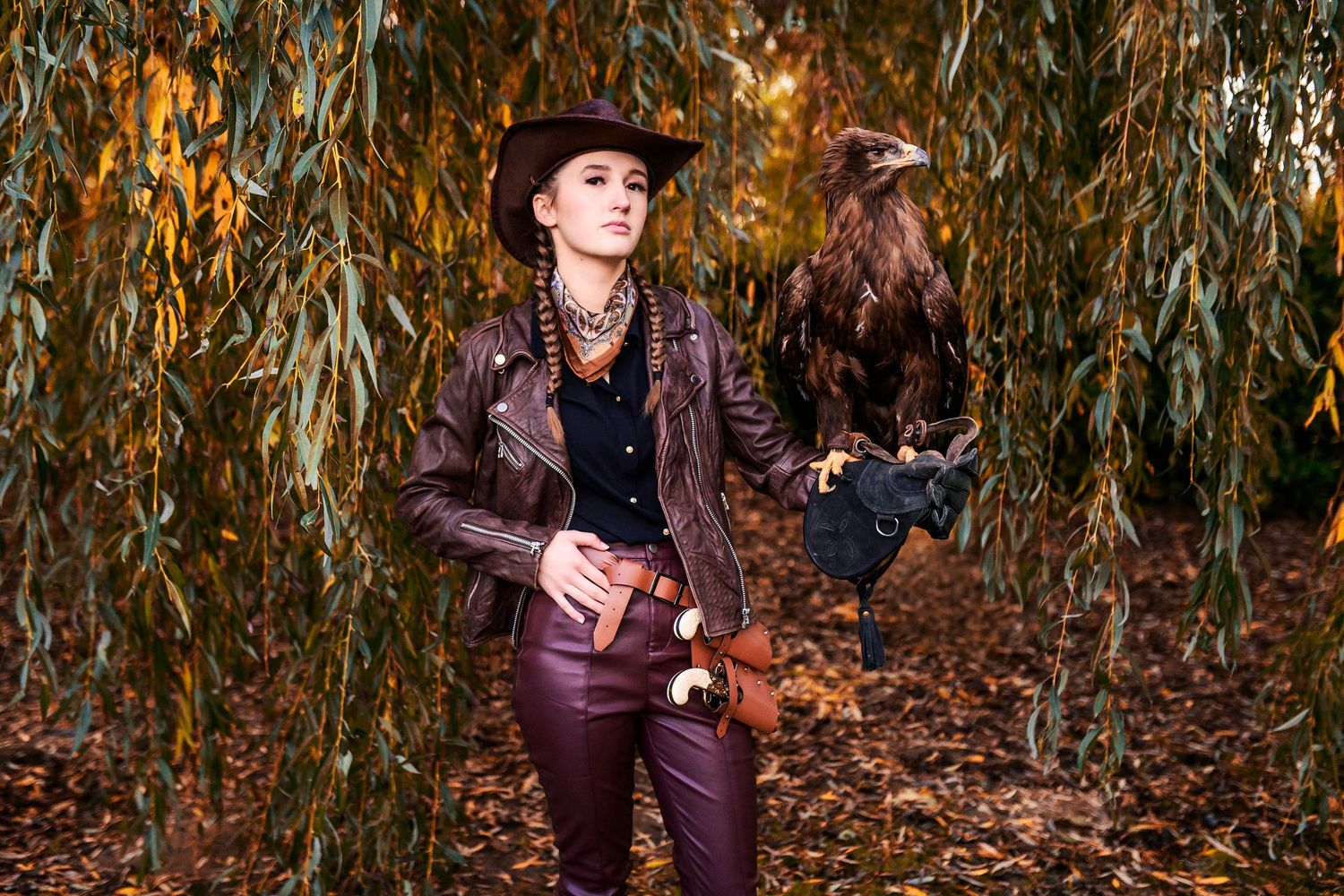 Falconer in rustic attire works with birds of prey among autumn corn stalks.