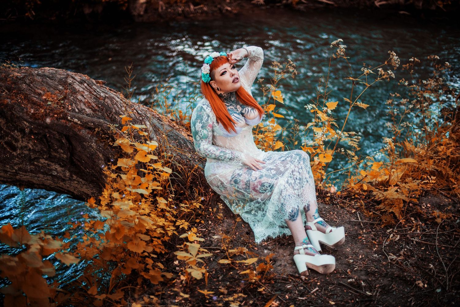 Figure in white dress reclining on tree branch over stream with autumn colors.