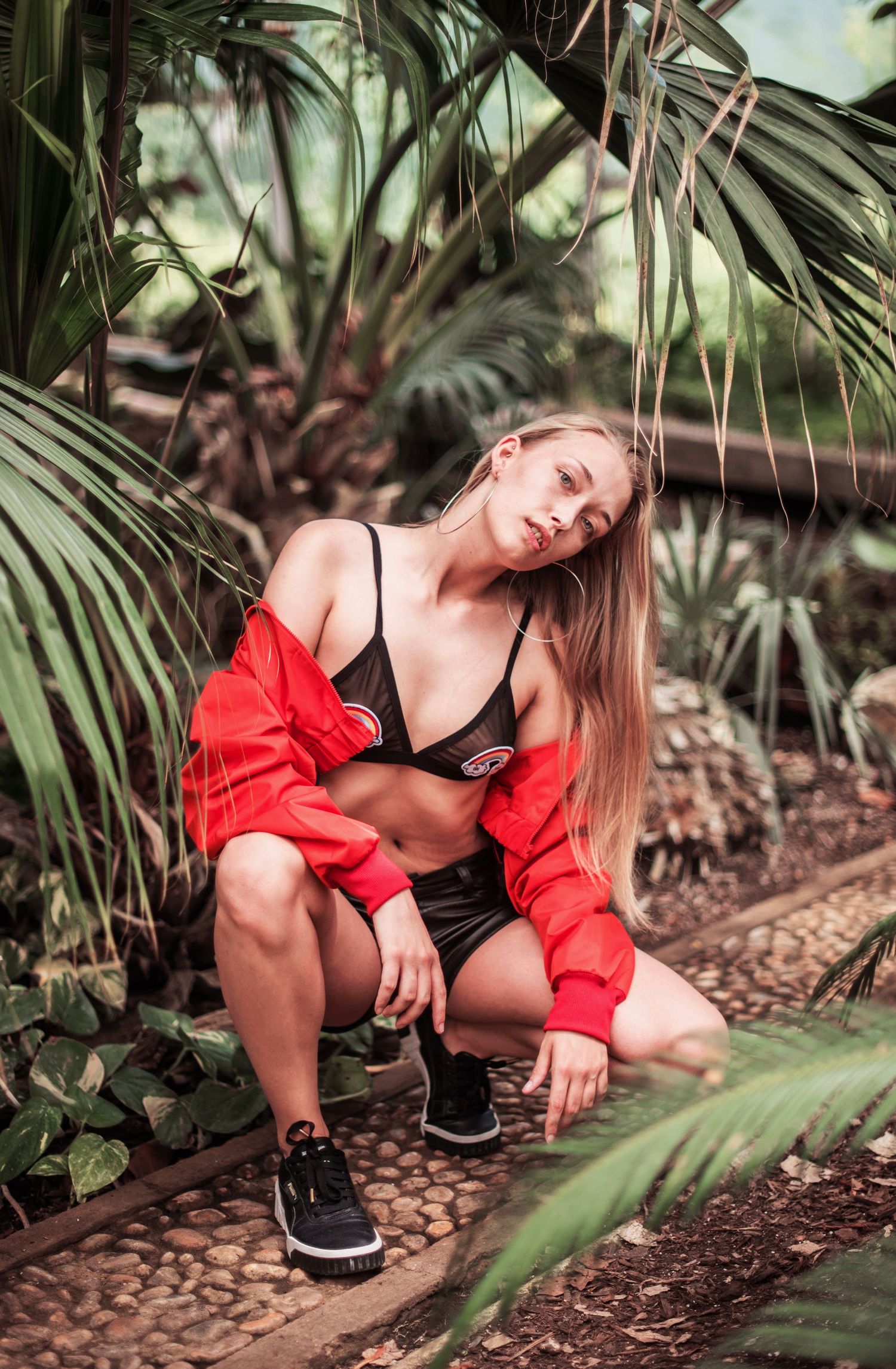 Fashion shoot among tropical plants with red jacket and black athletic wear.