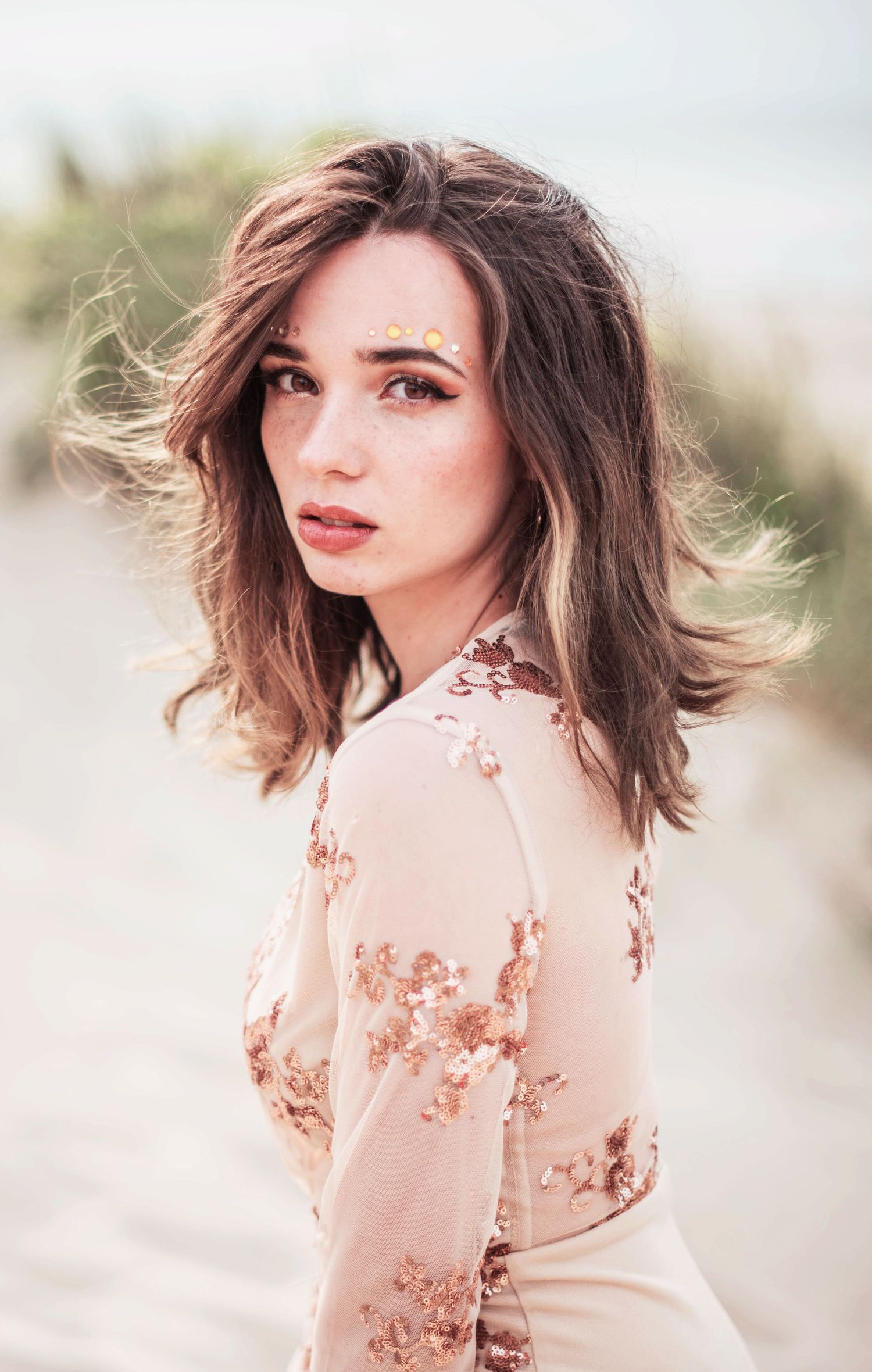 Portrait of a woman in a floral beige dress with windswept hair against a soft background.