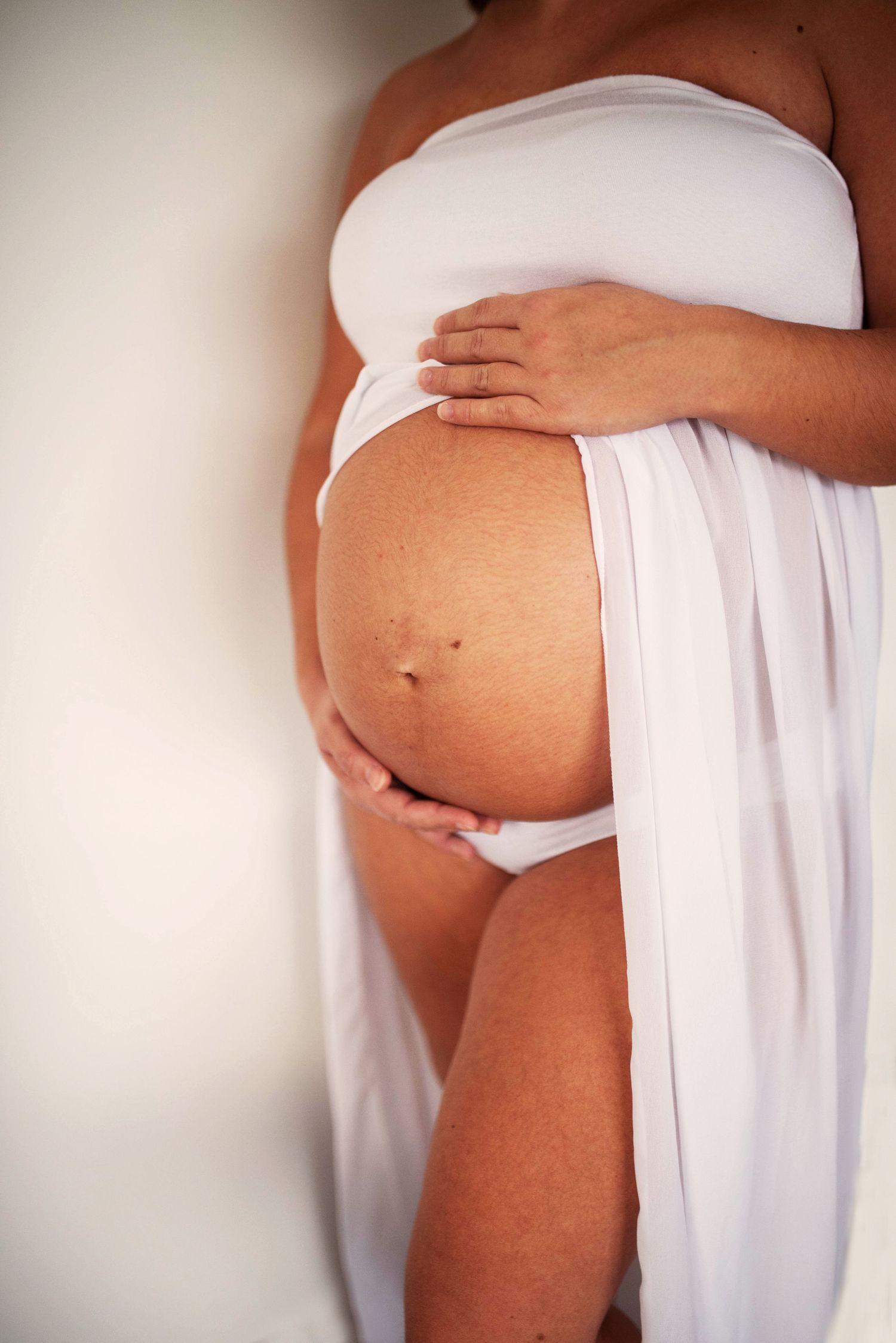 Artistic maternity photos showing pregnant belly draped in flowing white fabric.