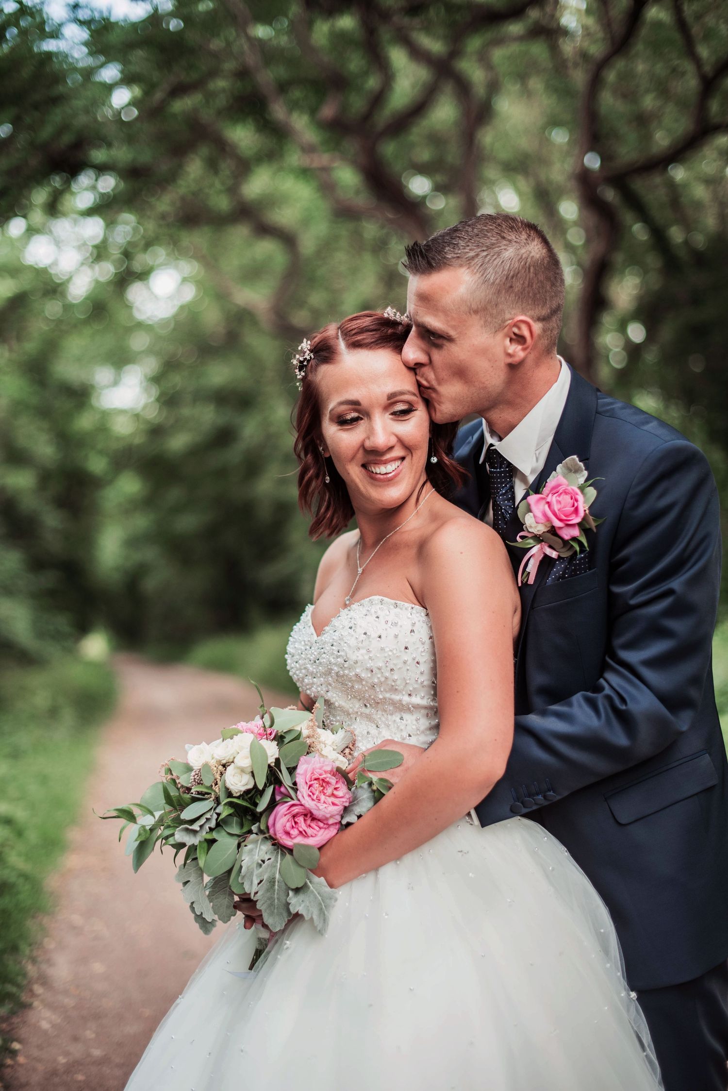 A candid wedding moment captured on a woodland path with pink rose bouquet details.