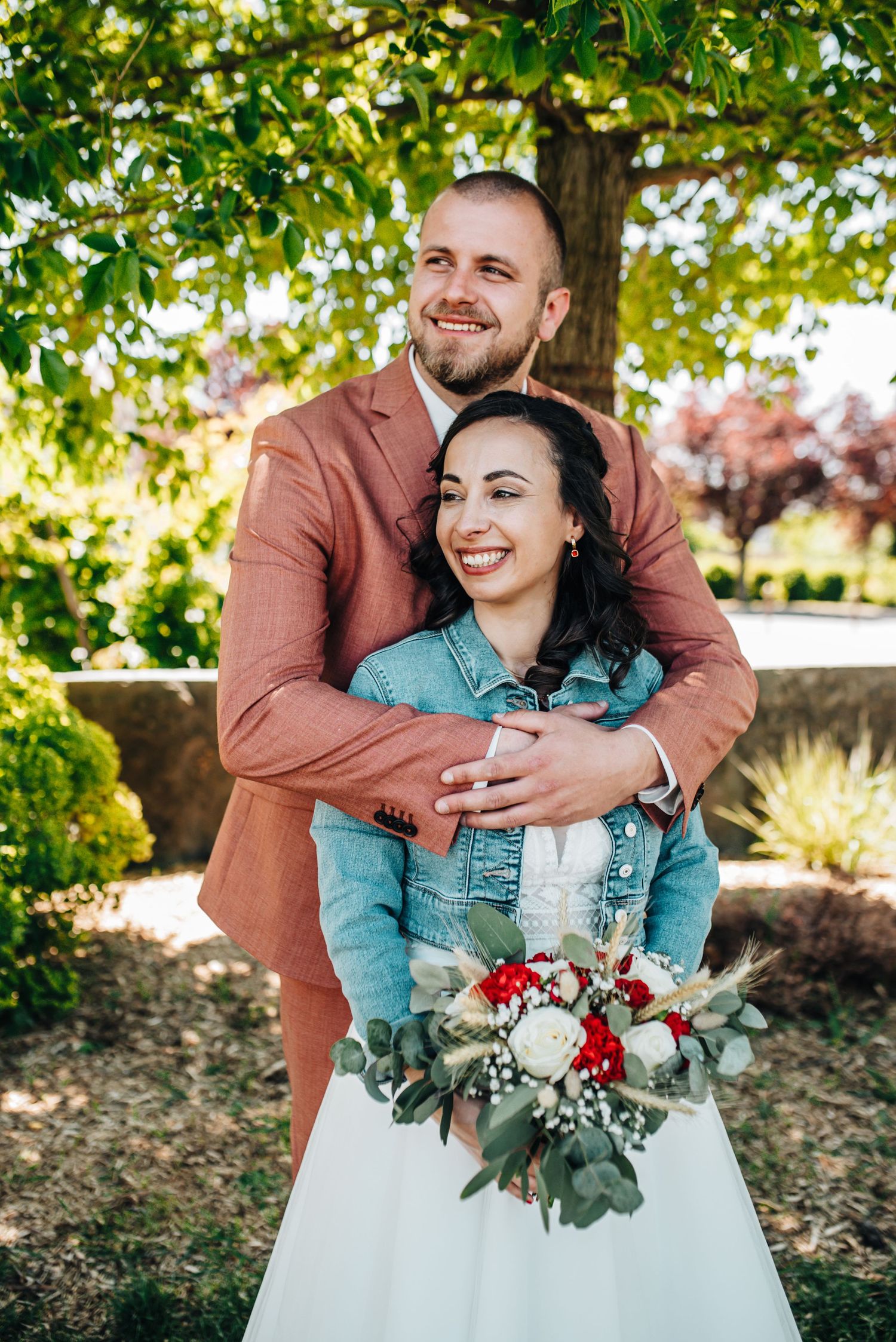 Wedding couple embracing outdoors with colorful floral bouquet and autumn foliage.