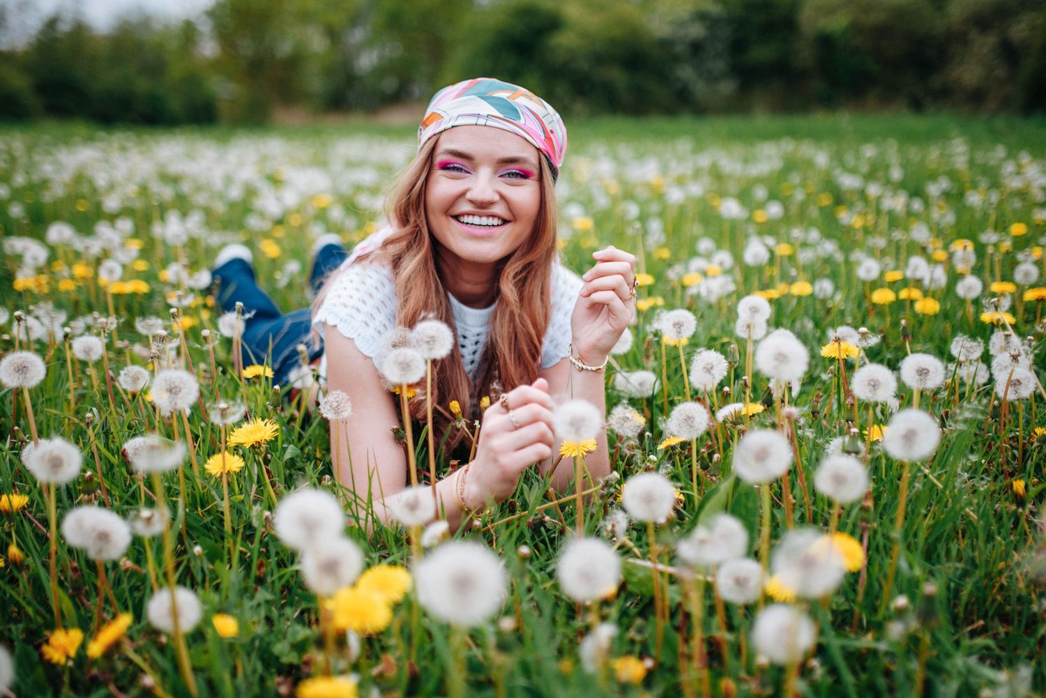 Person lying in field of dandelions and wildflowers on sunny day.
